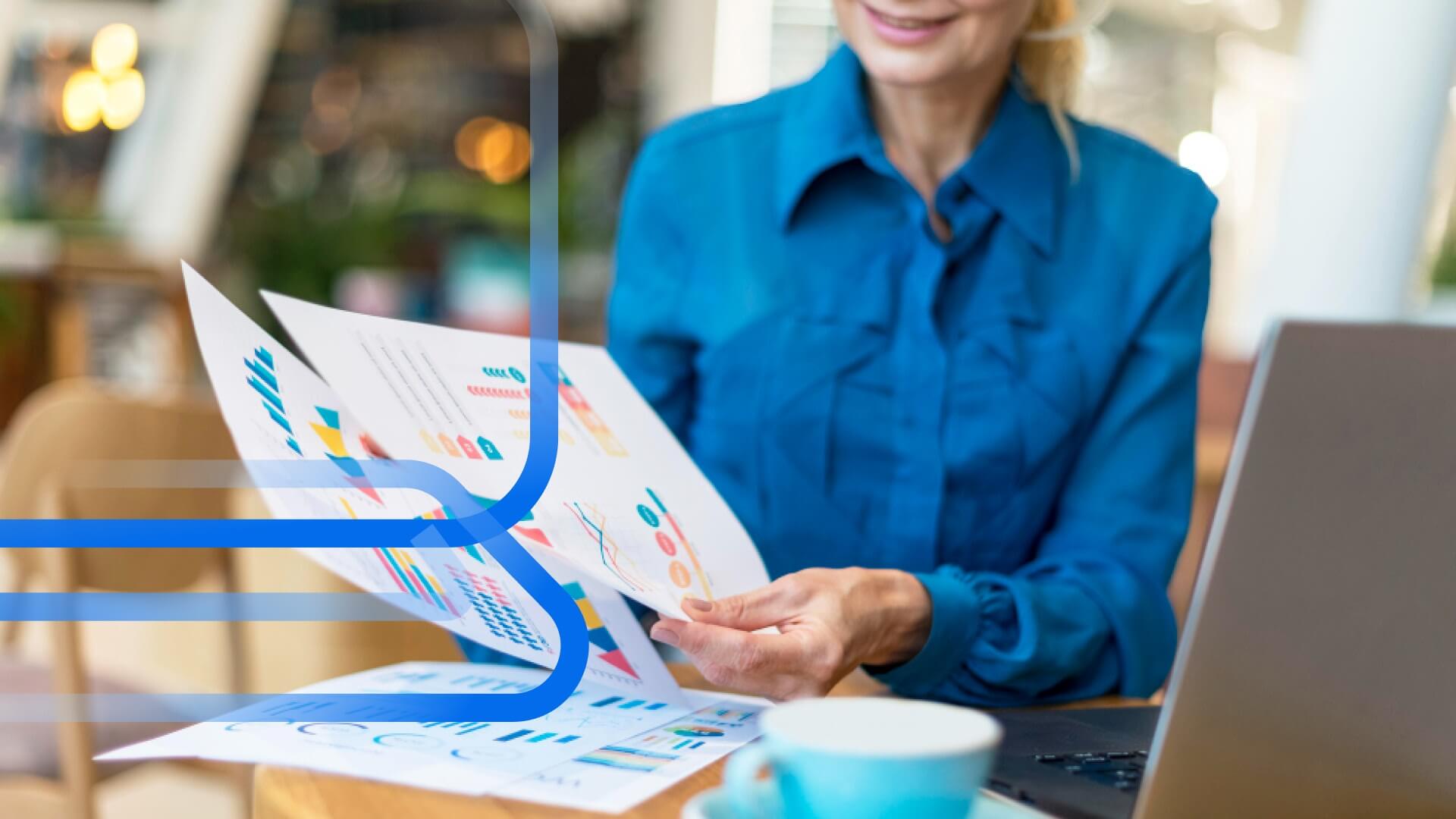 Profissional analisando gr&aacute;ficos e documentos em mesa de trabalho, representando a cria&ccedil;&atilde;o de um relat&oacute;rio de vendas para tomada de decis&atilde;o.