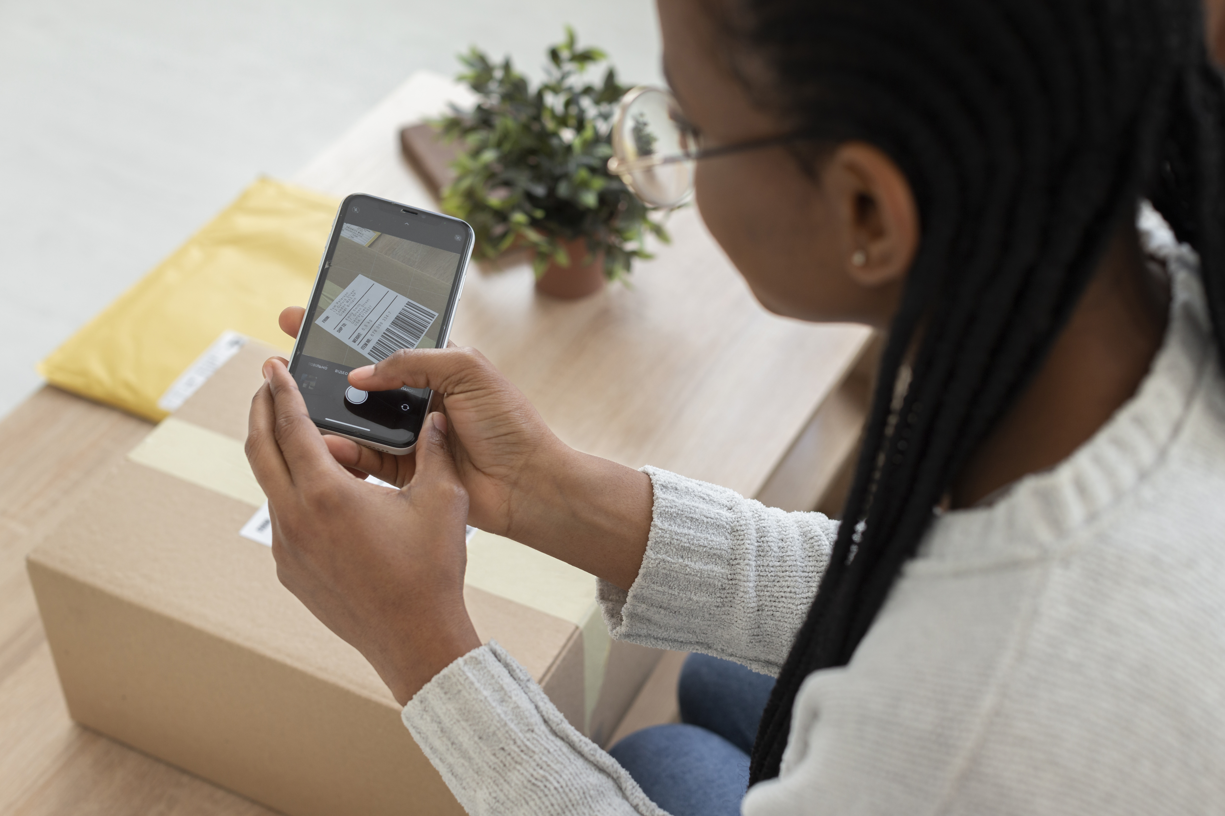 Pessoa fotografando etiqueta de envio com smartphone ao lado de pacote, ilustrando processo de envio para vender na Shopee.