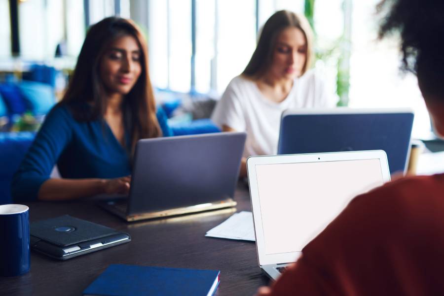 Três mulheres trabalhando com notebooks em uma mesa de reunião, representando equipe de atendimento no e-commerce