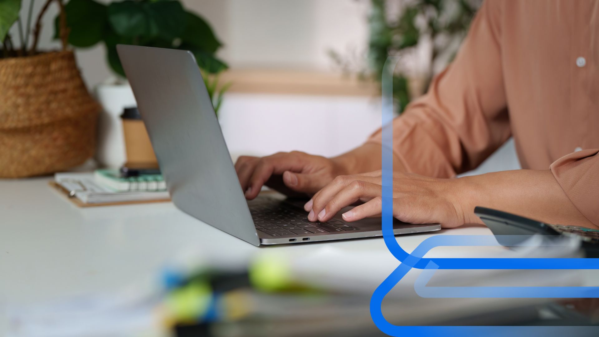 M&atilde;os digitando em laptop sobre mesa de escrit&oacute;rio com planta, caf&eacute; e design azul, representando efici&ecirc;ncia operacional na gest&atilde;o de marketplace