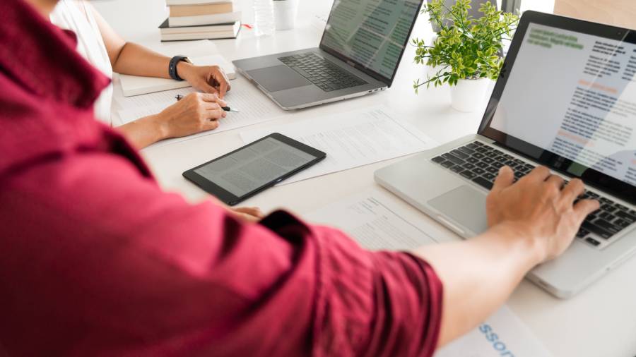 Duas pessoas trabalhando em uma mesa com notebooks, tablet e papéis, representando a eficiência operacional em operação de marketplace