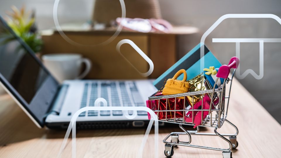Carrinho de compras em miniatura cheio de produtos ao lado de laptop, representando estratégia de anúncios em marketplace.