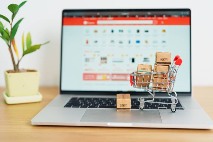 Laptop com site de e-commerce, carrinho de compras miniatura e caixas de entrega.