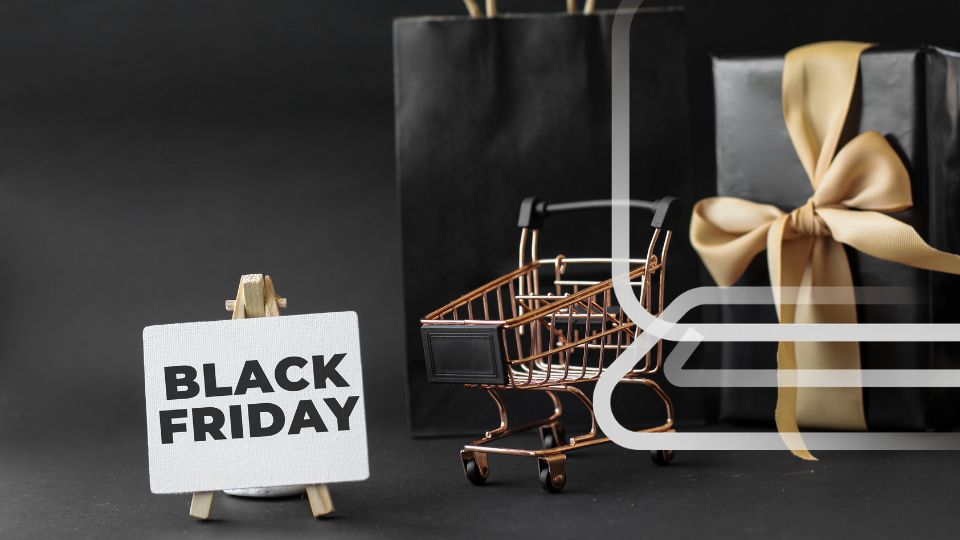 Sinal "Black Friday" em cavalete, carrinho de compras dourado, sacola e caixa de presente pretas.