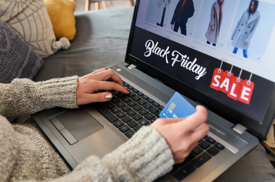 Pessoa fazendo compras online de Black Friday em um laptop, segurando um cartão de crédito.