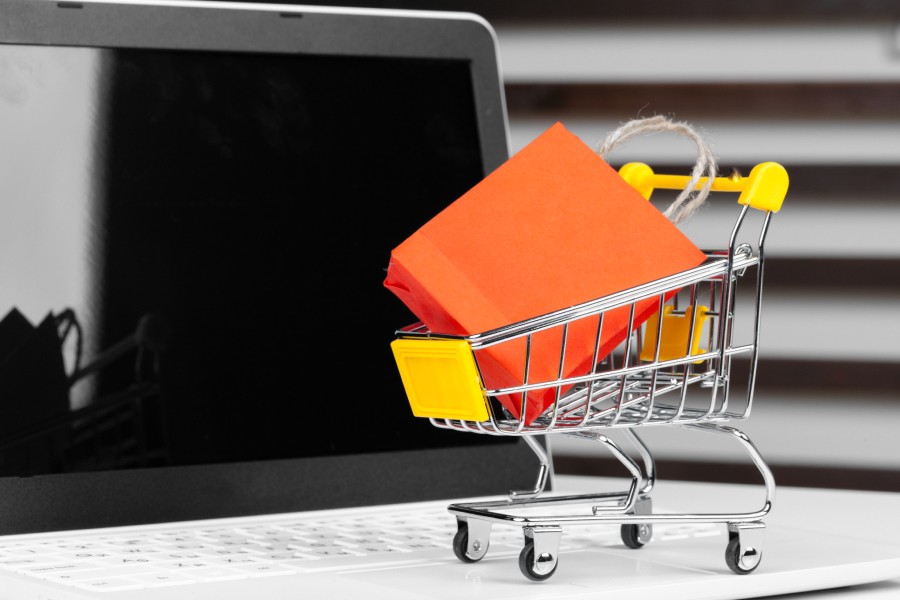 Mini carrinho de compras com sacola laranja sobre notebook, representando as tendências do Mercado Livre em e-commerce 